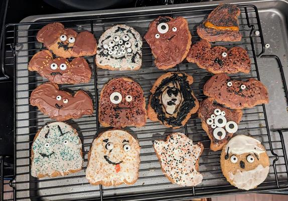 A cooling rack of halloween cookies. Theyre kind of goofy. Some have goody faces. A couple have 10-15 eyes.