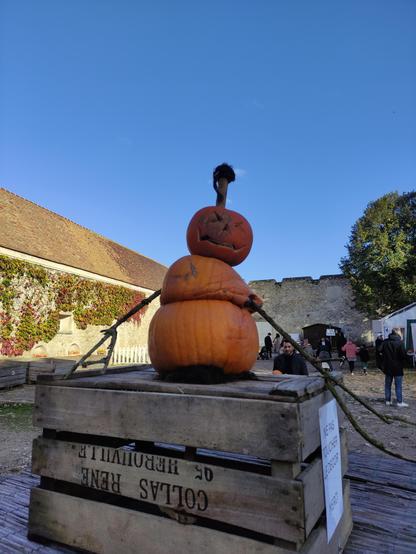 3 citrouilles mises les unes sur les autres comme un bonhomme de neige, agrémentées de bras en bois et a la figure abîmée