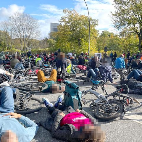 Mahnwache auf der gesperrten Hamburger Verbindungsbahn: Hunderte Radfahrende liegen neben ihren Fahrrädern auf der Straße und gedenken einer getöteten Radfahrerin.
