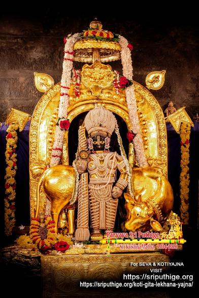 Idol of Hindu deity Krishna standing on gold-covered pedestal dressed in pearl "chain mail" (gold undergirding) and a matching dome-shaped crown, holding a similarly-clad staff in right hand. A string of white jasmine flowers around Krishna. A gilded cow behind Krishna with head turned back to gaze at Krishna's feet. A gold arch with broad sides around Krishna. Two gold flags and two flares pee from behind the arch. A small gold umbrella at the top of the arch. A string of white flowers (some red roses) hang down from the top of the umbrella on to both sides of Krishna. A string of green betel leaves (with a red rose and a yellow flower on each leaf) atop the umbrella.