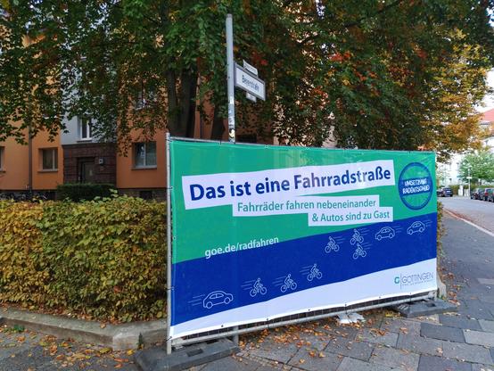 Großes Banner am Straßenrand: "Das ist eine Fahrradstraße. Fahrräder fahren nebeneinander und Autos sind zu Gast."