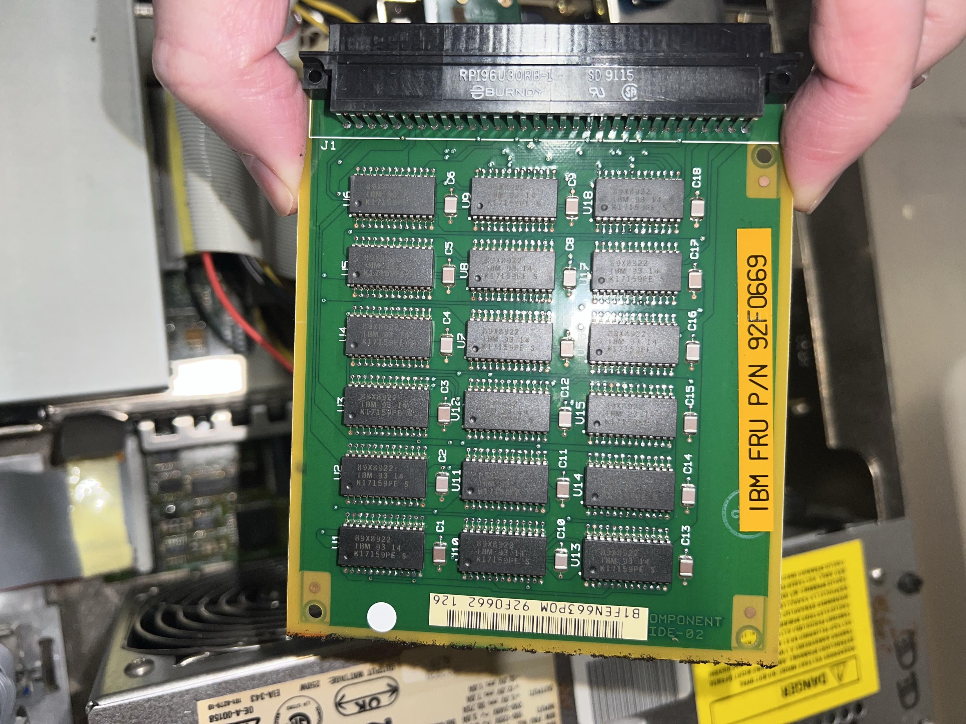 A hand holding a green circuit board with 3x6 rows of chips on it.