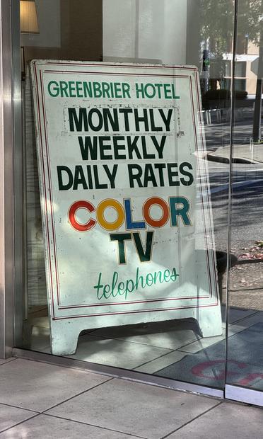 Sign of a local hotel, advertising monthly, weekly, and daily rates for rooms featuring television sets that support a spectrum of colours! Telephones are also available!