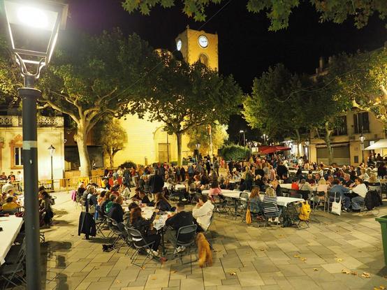 La plaça de l'església amb una gentada gaudint de la butifarra amb taules i cadires.