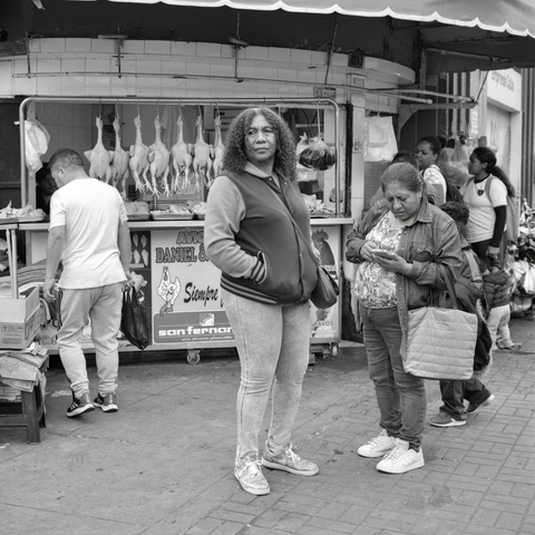 A black and white film photo. A woman appears to be focused on something out of shot while people jostle around her at a market on Jirón Cochrane in Lima, Peru. Thursday, September 18, 2025.
