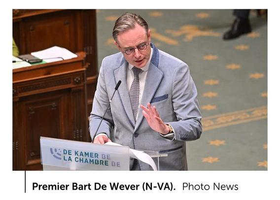 image/jpeg De Belgische premier Bart de Wever spreekt in de Kamer, gekleed in een blauwgrijs jasje met donkerblauwgrijze accenten, een wit overhemd en een zwart- of blauwwit geblokte das.