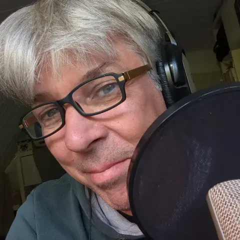 Ein grauer Mann mit Kopfhörern vor einem Mikrofon