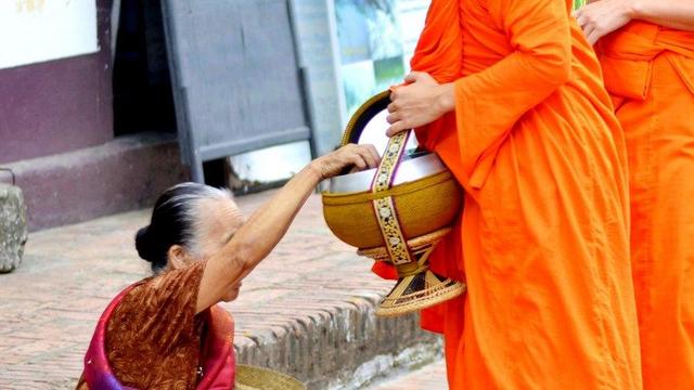 Person putting food in Buddhist monastic's bowl.