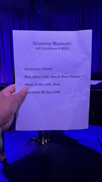 A hand holding a wrinkled music setlist for an event at the Grammy Museum featuring Jeff Goldblum and MSO. The setlist includes the songs "Manhattan," "Blue Minor," "Mean To Me," and "Everytime we say”