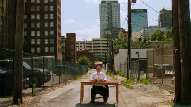 still of the documentary film "The Magic City - Birmingham According to Sun Ra" by Guillaume Maupin & Pablo Guarise - man sitting on a table with a microphone, in open air in an alley in Birmingham