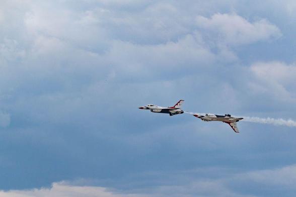 A U.S. Air Force Thunderbirds F-16 flies inverted while closely following another jet in level flight. Both aircraft trail smoke against a soft blue sky during an aerial demonstration at the Great Colorado Air Show in Loveland, Colorado.