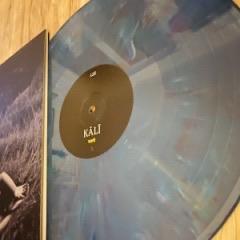 Eine Nahaufnahme einer blau marmorierten Schallplatte mit dem Titel "KALI", die teilweise neben dem Albumcover zu sehen ist.
