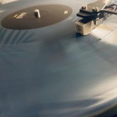 Nahaufnahme einer blauen Schallplatte auf einem Plattenspieler mit Tonarm und Tonabnehmer, die über der Oberfläche der Platte positioniert sind.