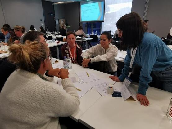 Cinq participants échangent autour d’une table pendant un atelier interactif de la Summer School sur la prise en charge des maladies neuromusculaires, documents de travail visibles.
