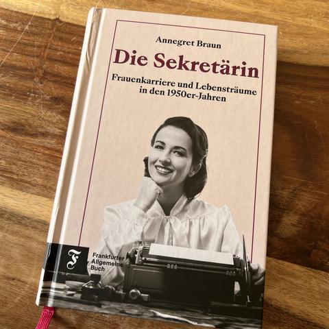 Titelbild des Buches "Die Sekretärin" von Annegret Braun. Das Bild zeigt eine Schwarzweiß-Aufnahme einer jungen Frau, die an einer Schreibmaschine sitzt. Auf dem Tisch neben der Schreibmaschine außerdem: eine Schreibfeder, ein Tintenfass, mehrere Stempel.