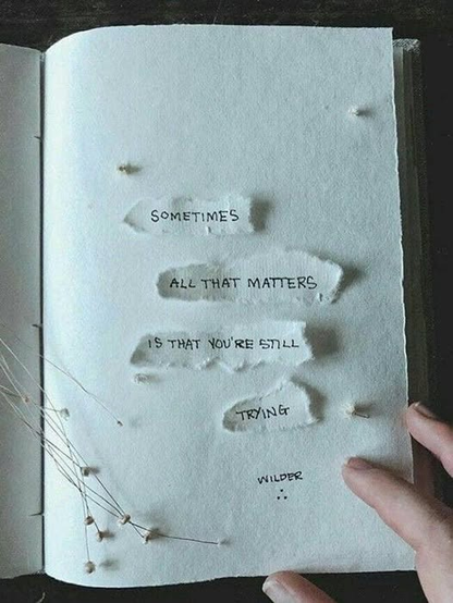 a person's hand on a page of a journal and ripped paper has words written on it "sometimess all that matters is that you're still trying - Wilder"