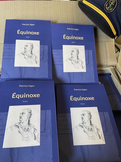carton contenant les exemplaires du roman "Équinoxe", casquette de marin en haut à droite.