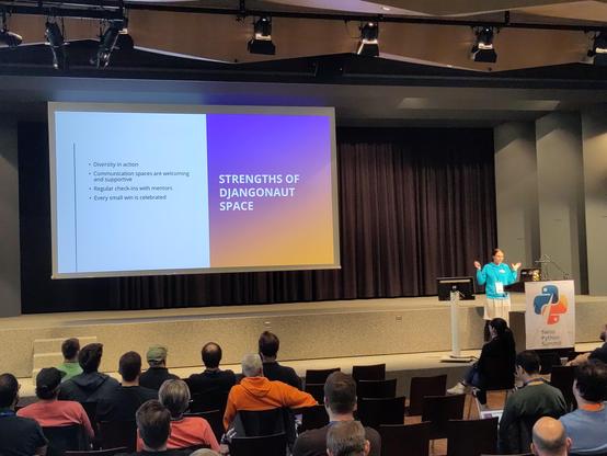 a pylady doing a lightning talk. slide says "strengths of djangonaut space"
