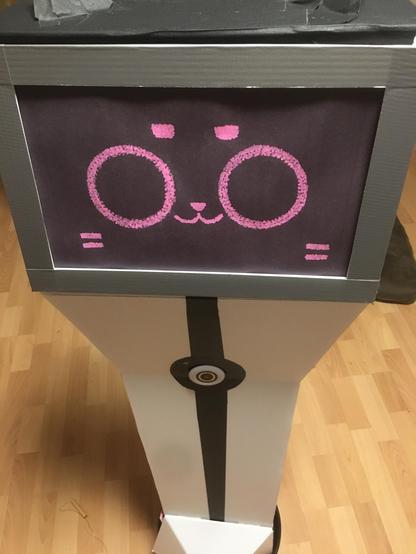 A real life, to-scale (about 4 feet-ish) Kerfur robot. It resembles a small, white pedestal with a camera in the middle of a back stripe, with pink accents and a screen displaying a cat face, with matching cat ears on top of the robot.