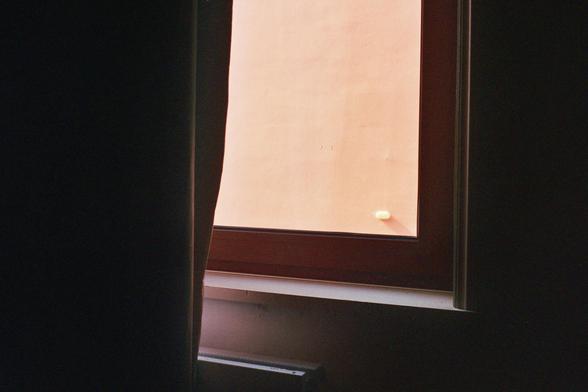 View through a window on a wall. The window is partly veiled by a curtain.