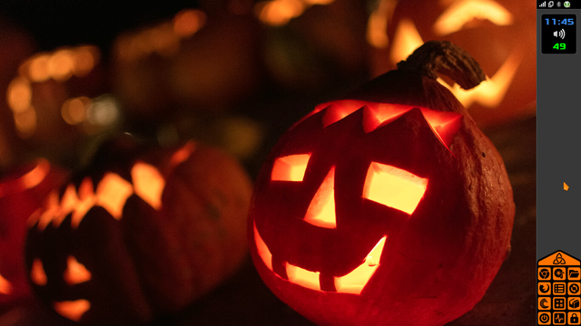 Fondo de escritorio con foto de calabazas de halloween iluminadas desde el interior, de modo que domina el color naranja vivo, con el naranja más apagado del exterior de las calabazas, y con los colores negros y oscuros del resto de la imagen, junto con el panel vertical en el lado derecho, en gris oscuro, con los iconos de los programas en el mismo color naranja y en negro, el reloj, el sensor de temperatura, el control de volumen y el área de notificación.