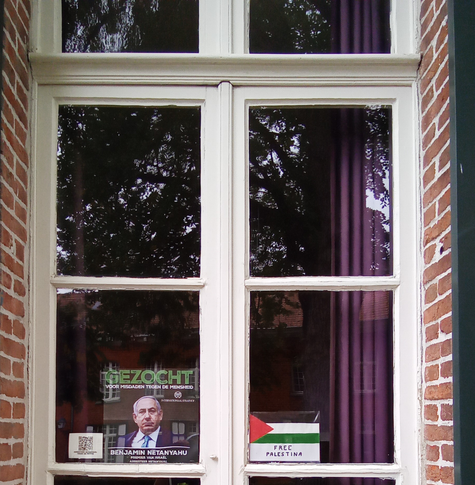 Une fenêtre avec une affiche en néerlandais disant "Recherché pour crimes contre l'Humanité" avec la photo de Benyamin Netanyahou. A côté, une affichette "Free Palestine" faite à la main.