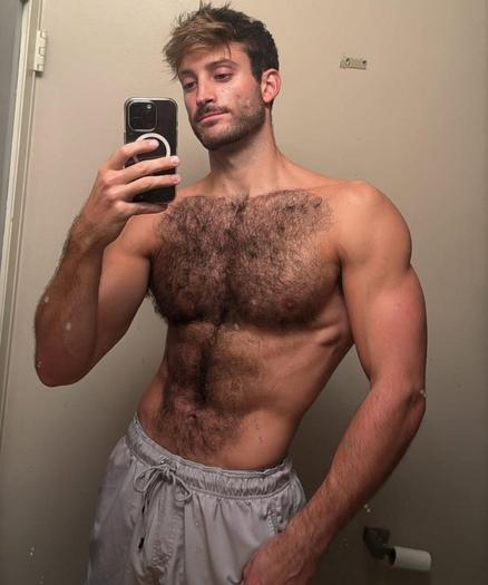A muscular man with a hairy chest is taking a selfie in a bathroom