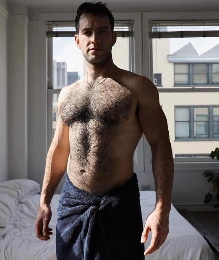 A hairy muscular man is standing in a room with a towel wrapped around his waist