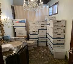Cardboard file boxes are piled 5-6 high in 7 disorganized columns. They are in a gaudily appointed bathroom