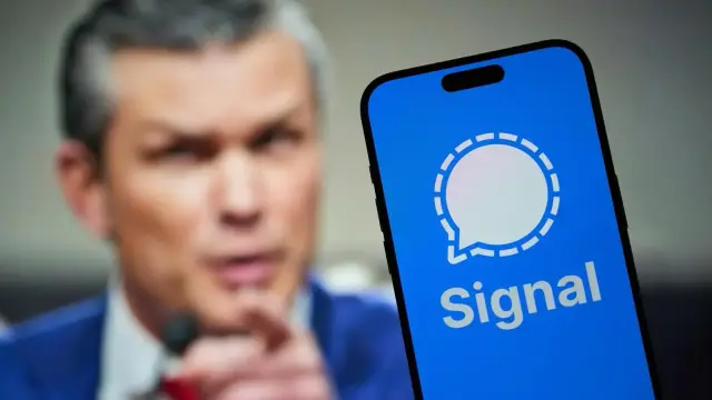 Hegseth (Middle-aged white male) is blurred in the background.  A phone with the signal app is in the foreground