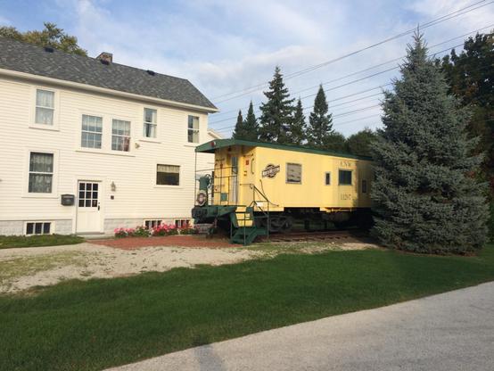 A yellow train car (a caboose) parked at a house.