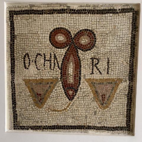 Mosaic of a stylised erect phallus with the tip pointing down, flanked by a vulva on each side, represented by a pubic triangle with a visible slit.
A coloured line points from the phallus' tip to the vulva on the left, suggesting some bodily fluid is involved.