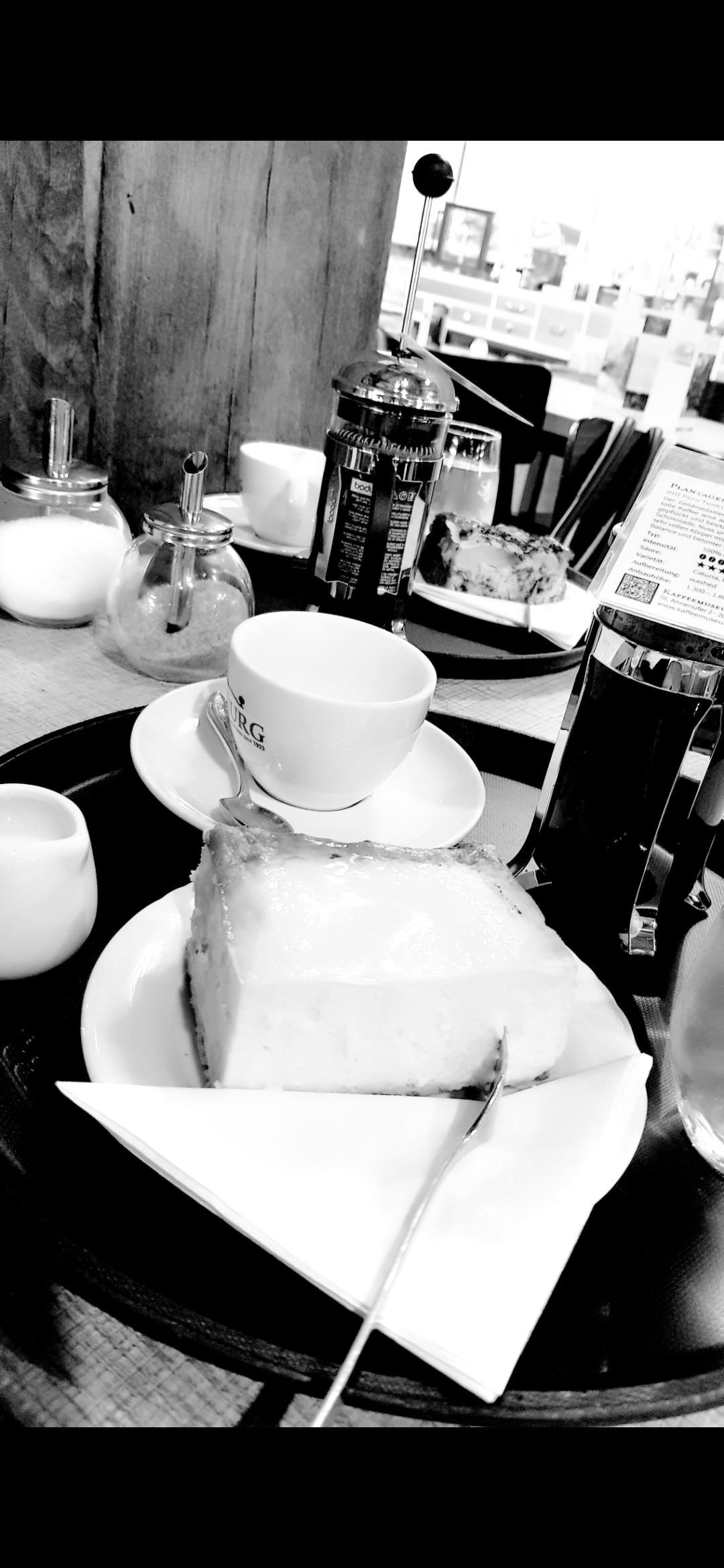 Schwarz-weiß Aufnahme eines Cafétisches in dutch angle mit Gedeck für 2 Personen mit Tassen, Kuchen und Kaffee in French press.