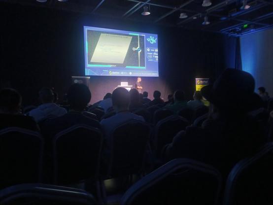 Photo of a darkened conference room with a big projected presentation and a speaker in the spotlight. The current slide is titled "2-5 километров полет", rest of the text rather unreadable.