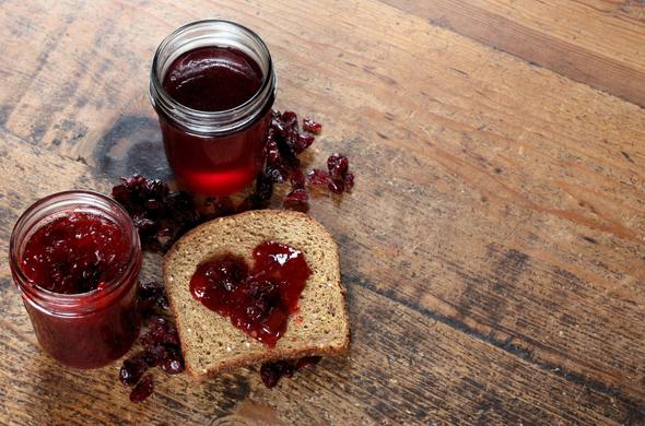 Two open jars of red jelly an a hearted shaped smear of jelly on a piece of brown bread