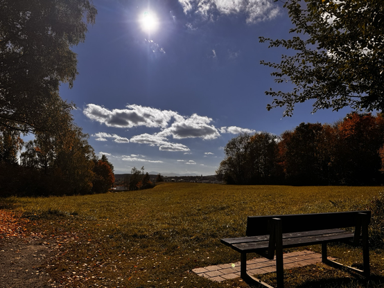 Eine Bank mit Aussicht auf Kaufbeuren, Alpenrand, Wolkenformation und strahlenden Sonnenschein blauer Himmel
