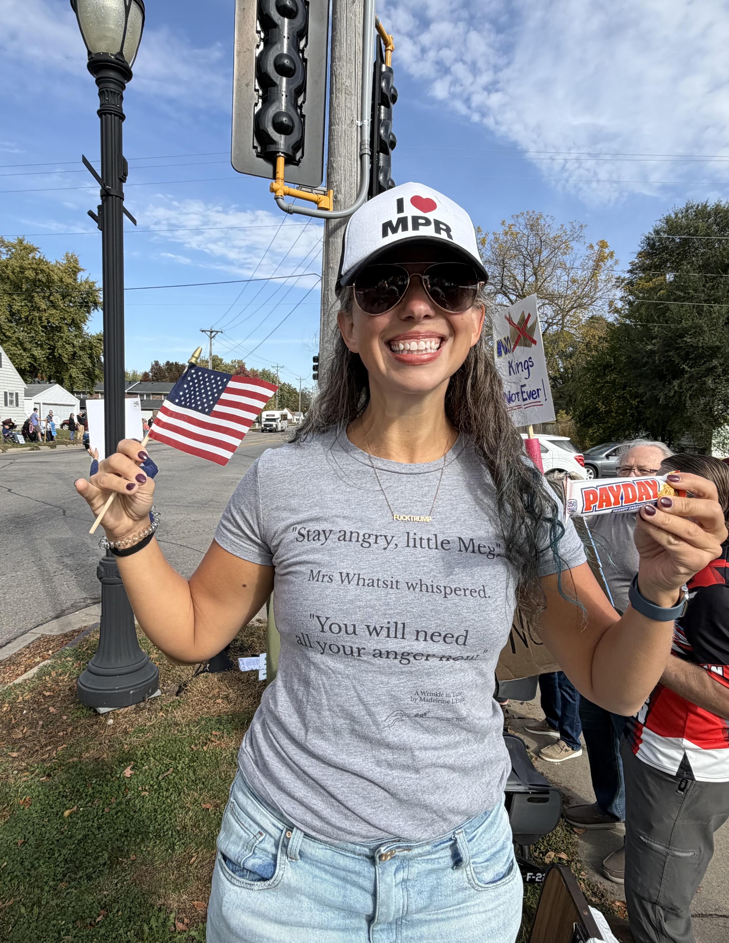 I’m holding an American flag and a payday candy bar. My hat says “I ❤️ MPR” and my shirt is a quote from A Wrinkle in Time, ‘“Stay angry, little Meg"
Mrs Whatsit whispered
"You will need
all your anger now’