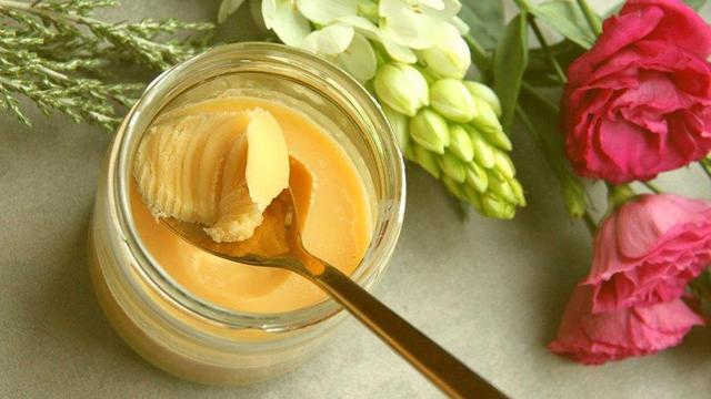 Photo of a jar of ghee with a spoon siting on a table surrounded by flowers.