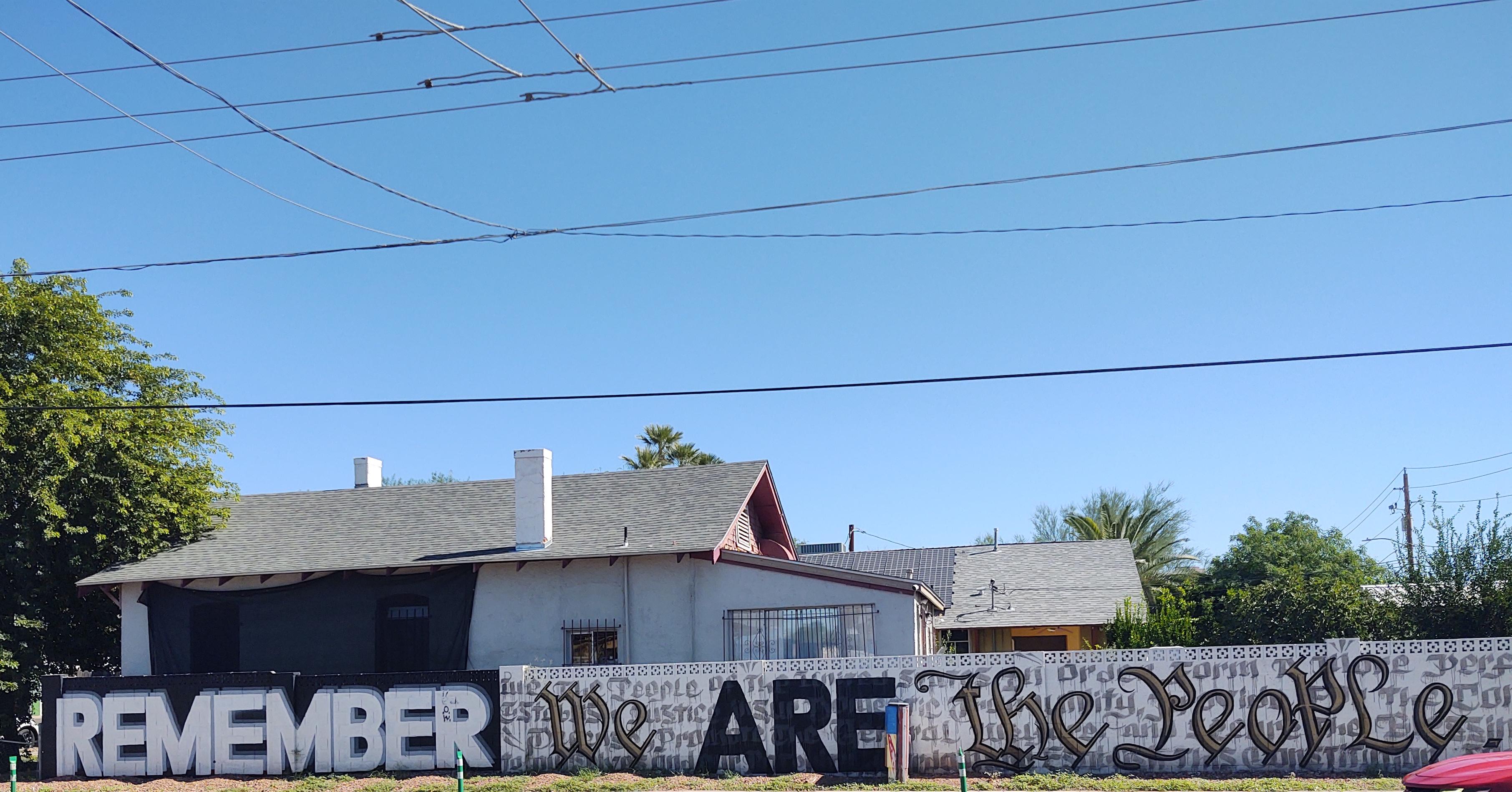 Wall around house stylistically painted to say, "Remember, we are the people"
