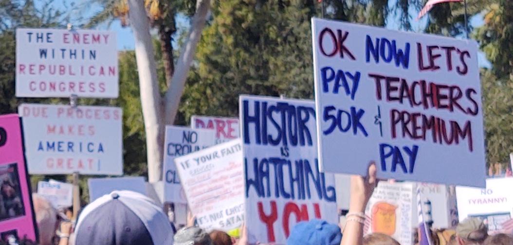 "OK, now let's pay teachers $50k and premium pay"
Another sign says "History is watching you"
Blurily further forward are signs for "The enemy within: Republican Congress" and "Due process makes America great"