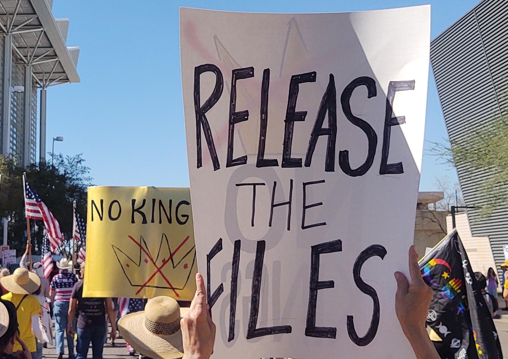 Signs that say, "Release the Files" and "No Kings", the latter has a crown with an x drawn over it