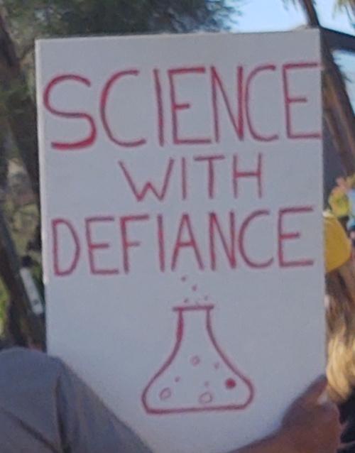 Sign says, "Science with Defiance" and has a drawing of a bubbling beaker