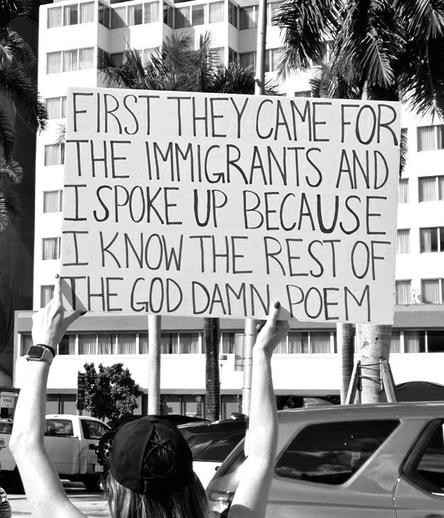 Demonstrantin hält Schild mit der Aufschrift: „FIRST THEY CAME FOR THE IMMIGRANTS AND I SPOKE UP BECAUSE INKNOW THE REST OF THE POEM“