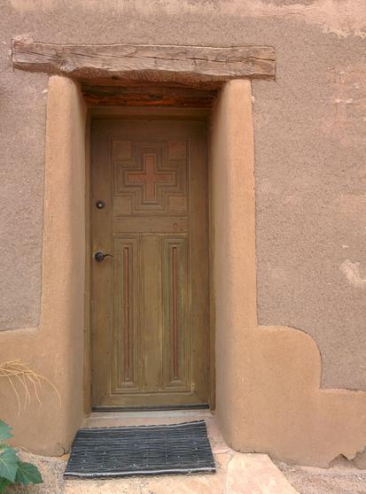 Image: Close up view of a warm beige and brown doorway with adobe plaster and wood details at The Tower Gallery in Pojoaque, New Mexico.