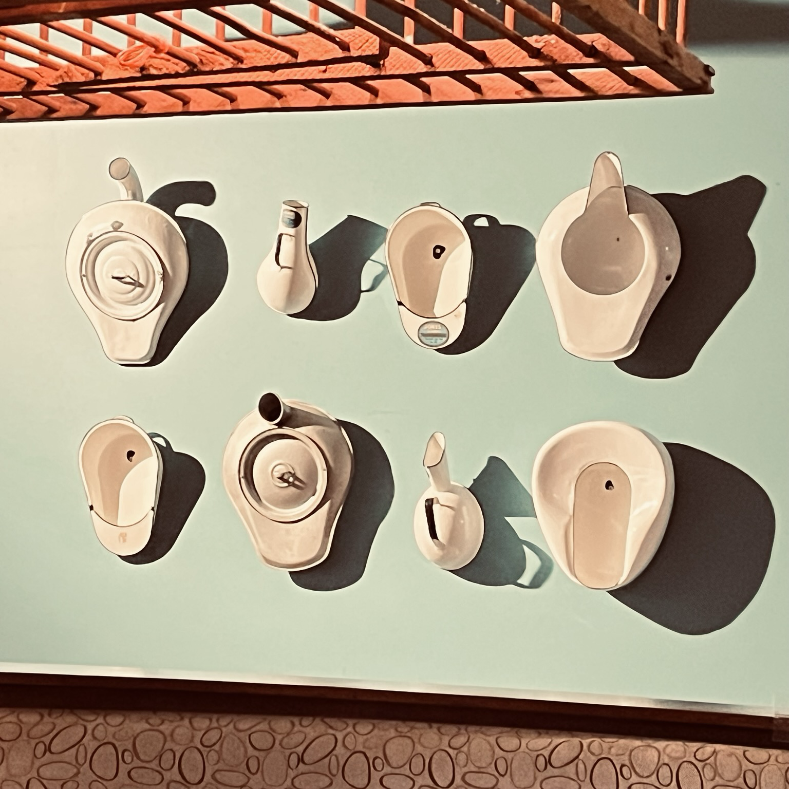 Two rows of starkly lit old-fashioned toilet bowls hang on a teal wall