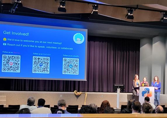 three pyladies talking on the swiss python summit conference stage. the presentation slide says "get involved!" and shows qr codes for pyladies zurich on meetup, mastodon and linkedin