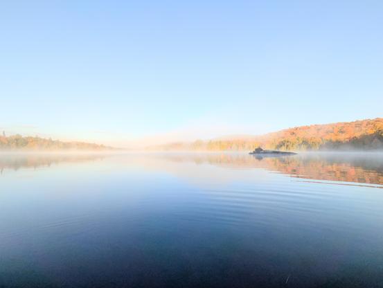 Soft morning fog blankets the lake, with hints of autumn colors on the shore.