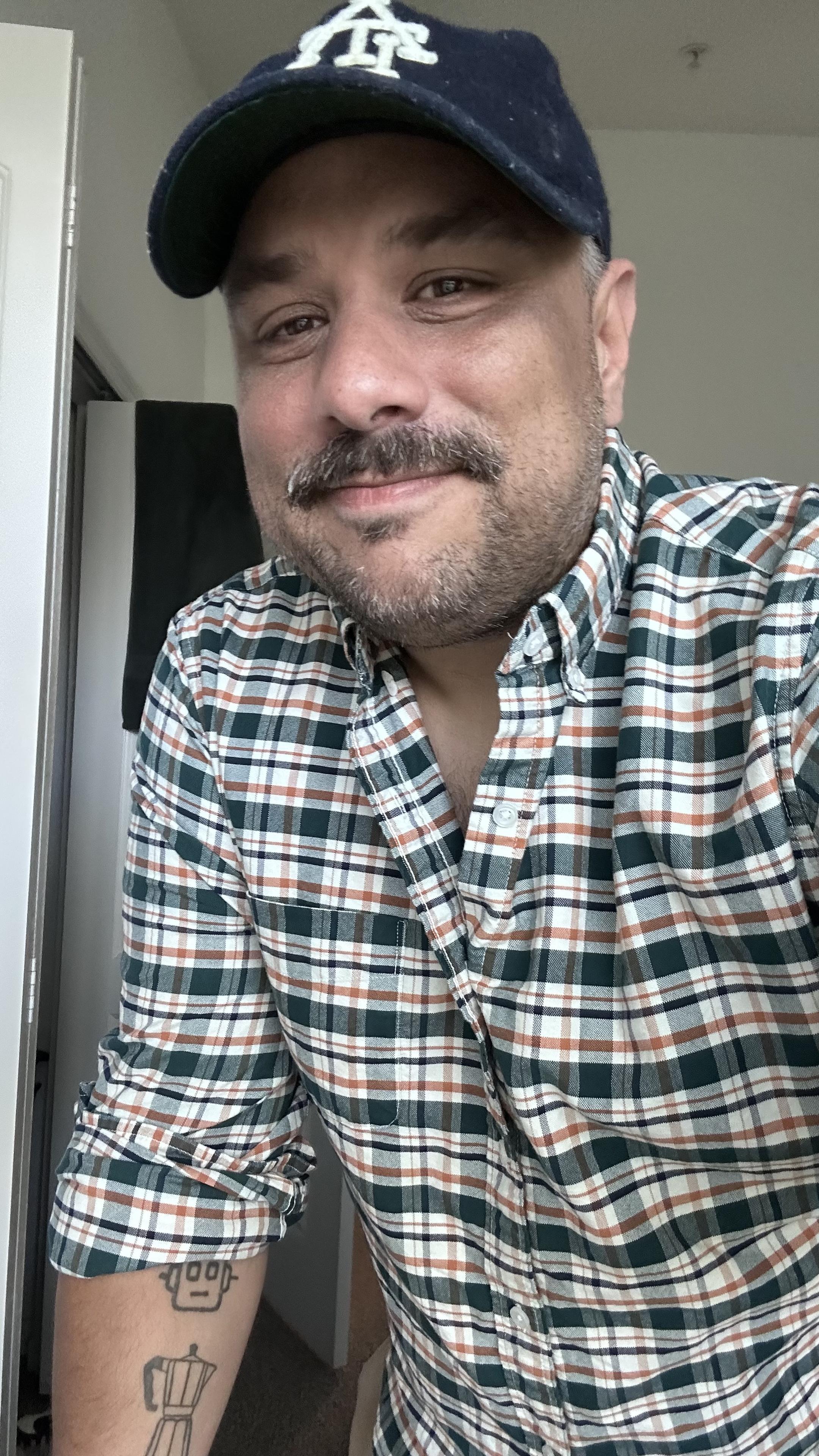 Me in a plaid shirt. It's green and orange and white. I'm wearing a blue baseball hat with ATL logo on it. 