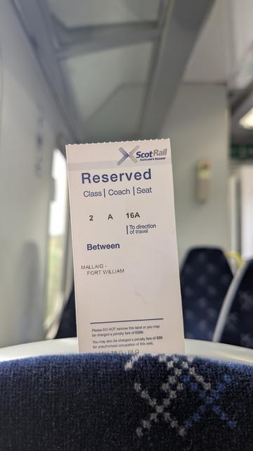 Reservation paper slip with text:
"Reserved
Class | Coach | Seat
2 A 16A
To direction of travel, between MALLAIG-FORT WILLIAM
Please DO NOT remove this label or you may be charged a penalty fire of £200.
You may also be charged a penalty tara of £50 for unauthorised occupation of this seat."
