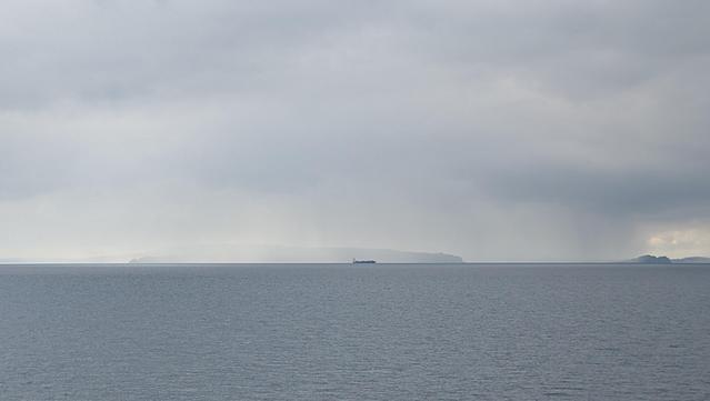 View of the sea, a ship in the distance, a rain front covering the sight of the shore
